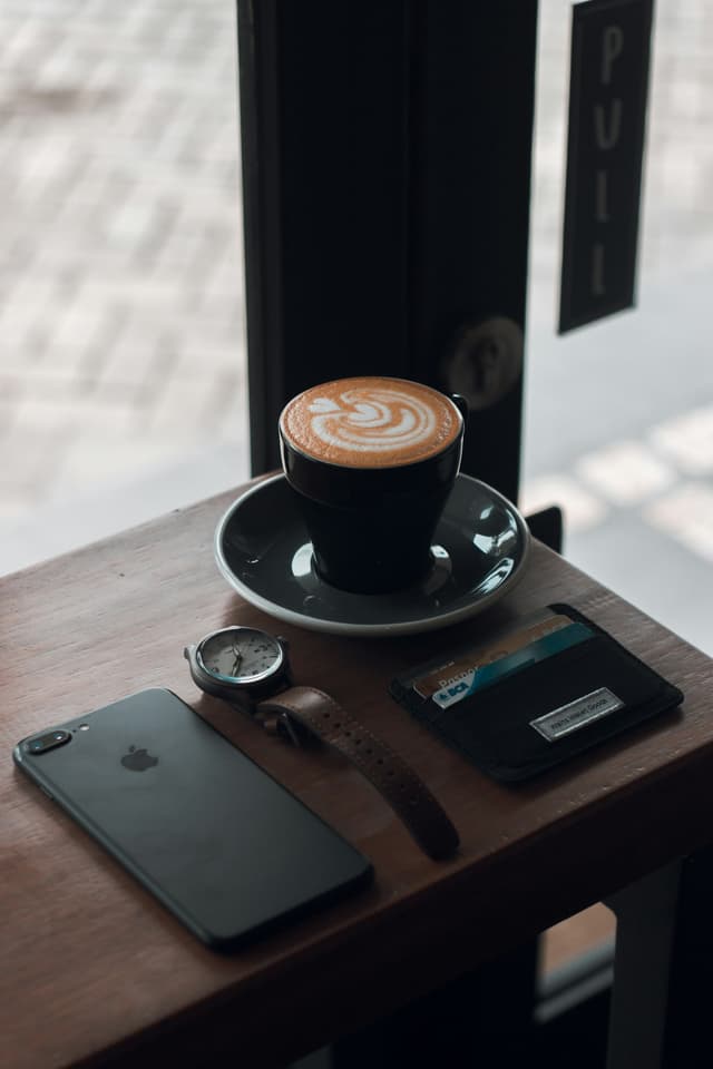 Coffee latte on a saucer beside an iPhone on a wooden table